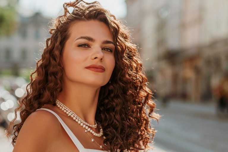 pretty curly haired brunette wearing layered pearl necklaces in a city street